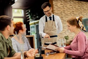 Smiling waiter taking the order of happy customers in a restaurant, highlighting customer service and dining experience at Workvantage.