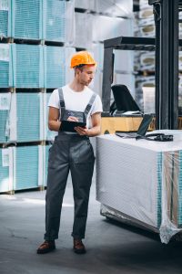 Warehouse worker using a laptop and taking notes, highlighting Workvantage's staffing and technological management services in manufacturing and warehousing.