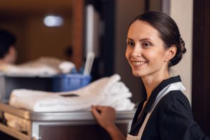 Smiling housekeeping employee with a supply cart in a hotel, highlighting dedication and service in the hospitality industry at Workvantage.