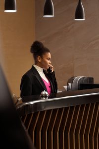 Professional receptionist answering a phone call at the front desk of a modern hotel, highlighting customer service and efficiency in the hospitality sector at Workvantage.