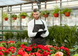Greenhouse worker inspecting flowers with a clipboard, highlighting the specialized staffing solutions for floriculture and greenhouse management provided by Workvantage.