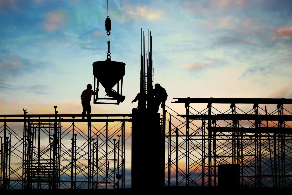 Silhouette of construction workers on scaffolding at sunrise, performing structural construction tasks, highlighting Workvantage's specialized staffing solutions.