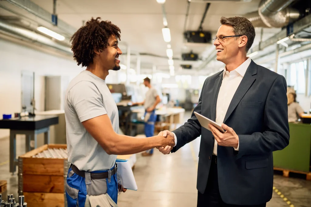 happy-engineer-young-black-worker-handshaking-while-greeting-industrial-building A factory worker shaking hands with a business manager, symbolizing successful collaboration. Workvantage provides staffing solutions that connect skilled workers with employers in various industries.