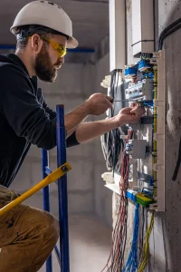 Electrician performing specialized skilled trades work on an electrical panel with precision tools.