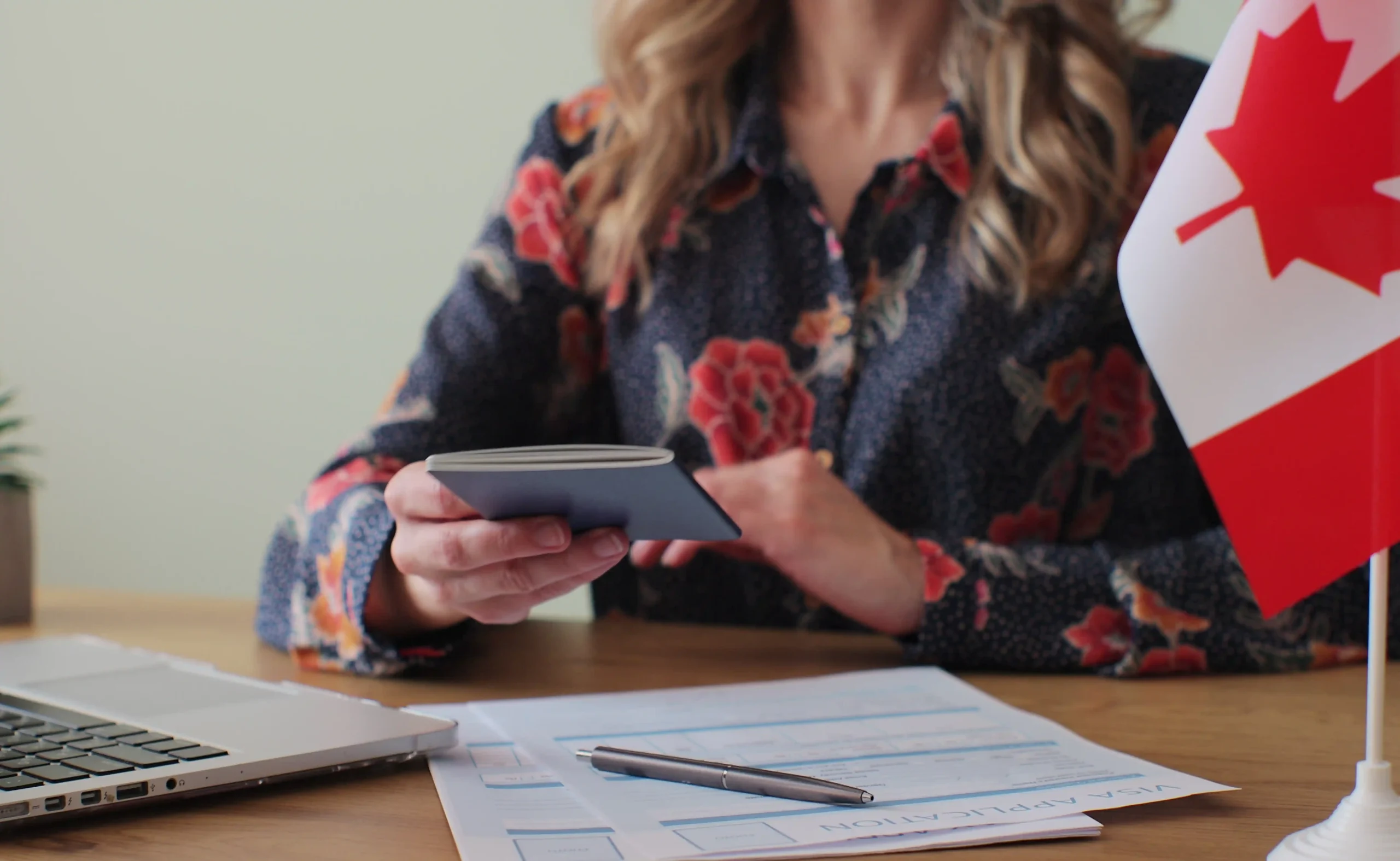 A person holding a passport, with Canadian immigration forms on the desk and a Canadian flag, illustrating Workvantage's support in managing LMIA applications and renewals for foreign workers.