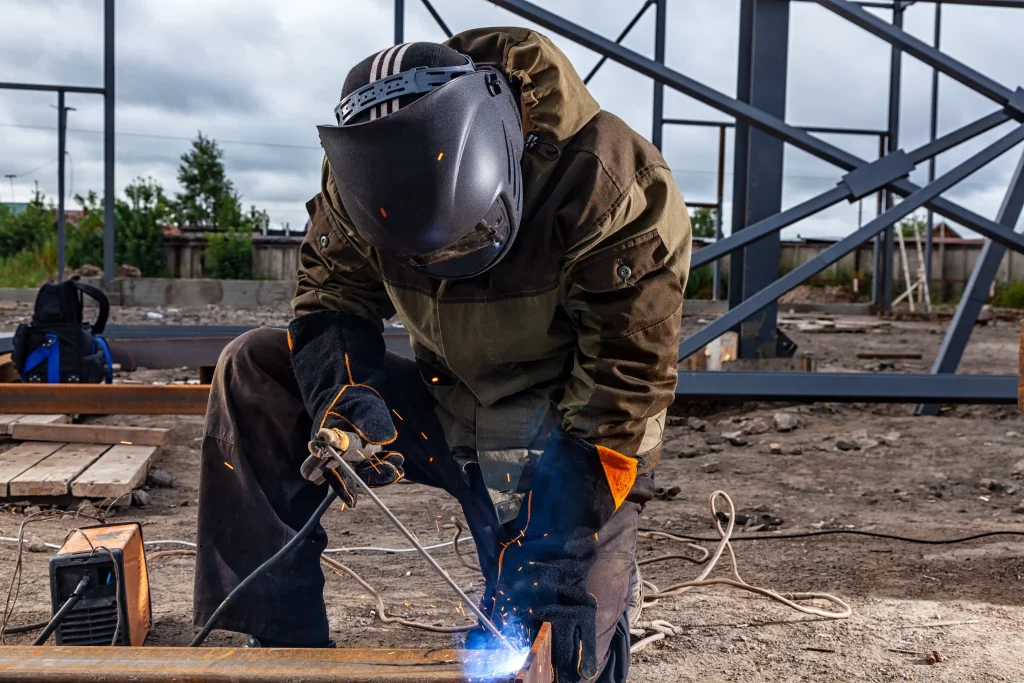 close-up-welder-weld-metal-pipe-construction-site-builder-brown-uniform-welding-mask-welders-leathers-weld-metal-with-arc-welding-machine-blue-sparks-fly-sides Industrial worker performing welding at a construction site. Workvantage offers skilled industrial workers and tradespeople to help companies in construction, manufacturing, and other industrial sectors meet their staffing needs.