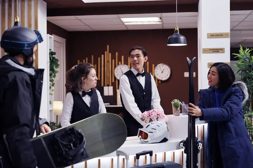 Hotel staff assisting tourists with ski equipment, illustrating hospitality and customer service at a winter resort.