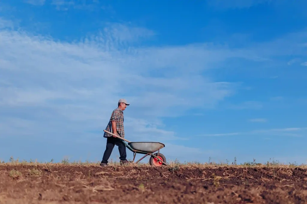 Agriculteur travaillant la terre avec une brouette, représentant la résilience agricole face aux défis d'urbanisation et de durabilité.