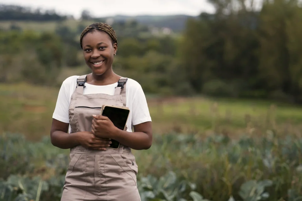 Jeune femme agricultrice souriante tenant une tablette dans un champ, représentant l'innovation et les pratiques agricoles durables soutenues par Workvantage.